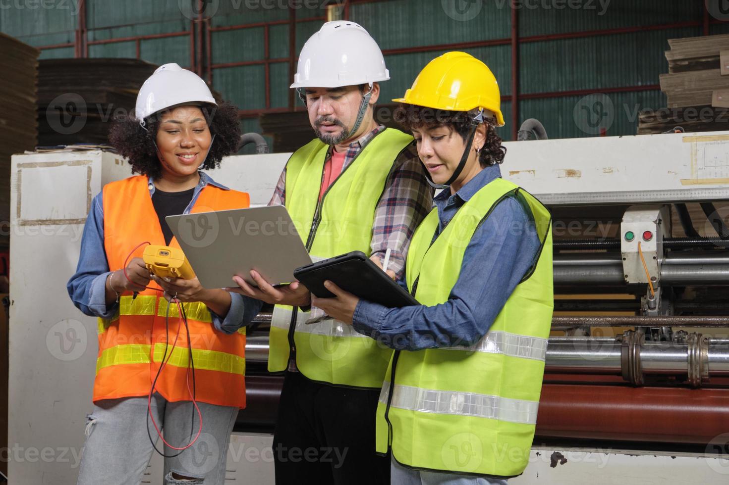 Safety uniform workers and industrial engineers with hardhat use laptop computer to check and control machines. Three professionals work in paper manufacturing factory, maintain production equipment. photo