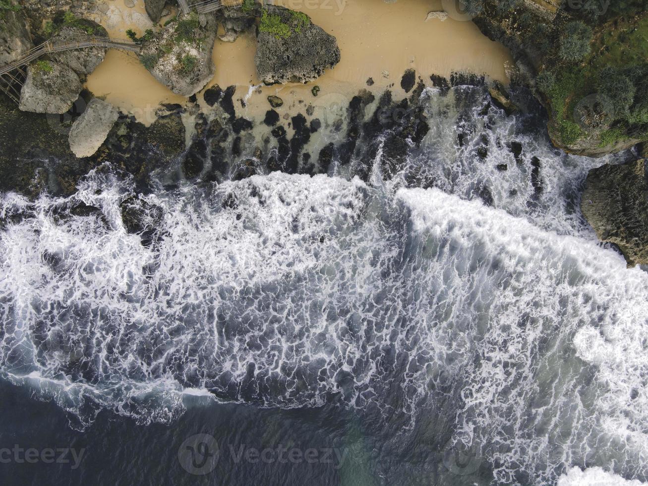 Top down aerial view of giant ocean waves crashing and foaming in coral beach photo