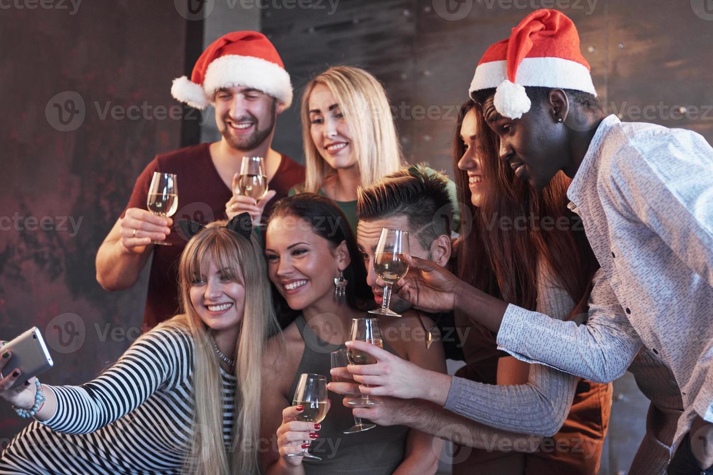 Group beautiful young people doing selfie in the new year party, best friends girls and boys together having fun, posing emotional lifestyle people. Hats santas and champagne glasses in their hands photo