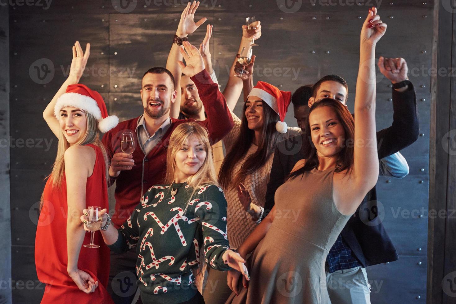 fiesta con amigos. aman la navidad. grupo de jóvenes alegres que llevan bengalas y copas de champán bailando en la fiesta de año nuevo y mirando felices. conceptos sobre el estilo de vida de la unión foto