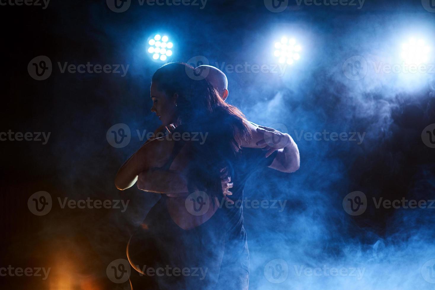 hábiles bailarines actuando en la habitación oscura bajo la luz y el humo del concierto. pareja sensual realizando una danza contemporánea artística y emocional foto