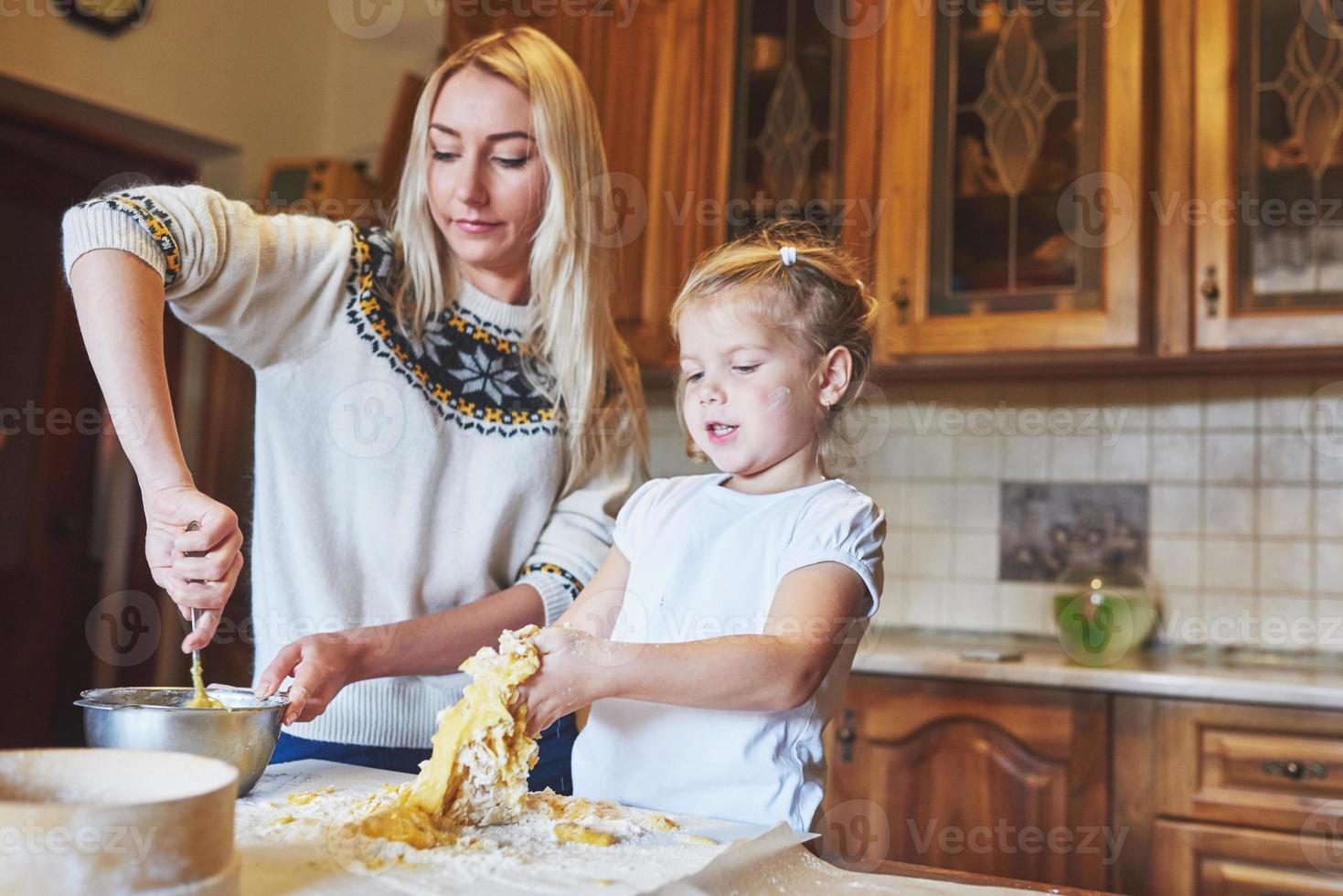 feliz mamá sonriente en la cocina hornea galletas con su hija. foto