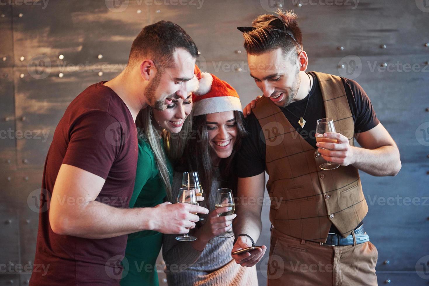 alegres viejos amigos se comunican entre sí y miran el teléfono, con copas de champán en la fiesta de año nuevo. concepto de entretenimiento y estilo de vida. personas conectadas wifi foto