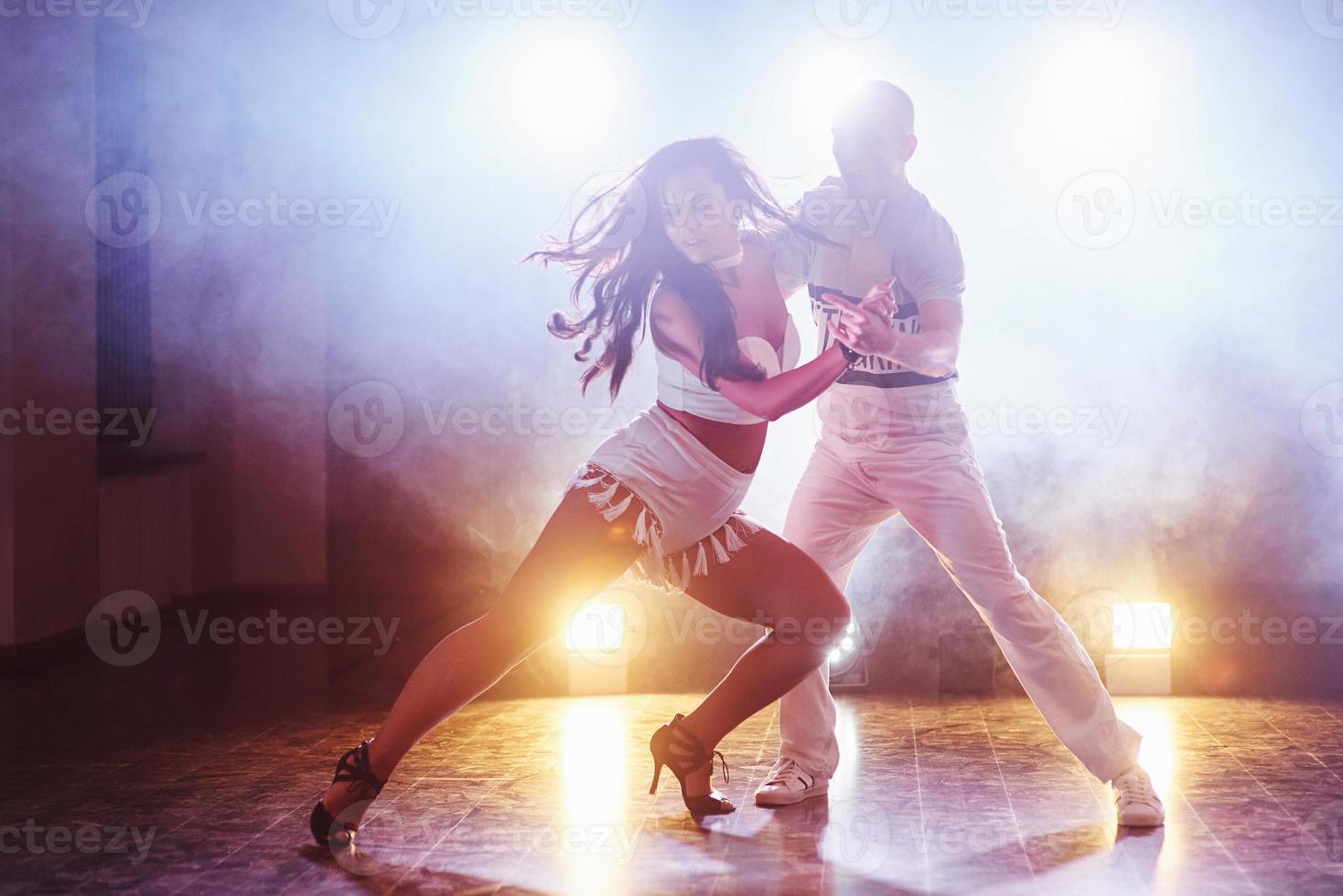 hábiles bailarines actuando en la habitación oscura bajo la luz y el humo del concierto. pareja sensual realizando una danza contemporánea artística y emocional foto