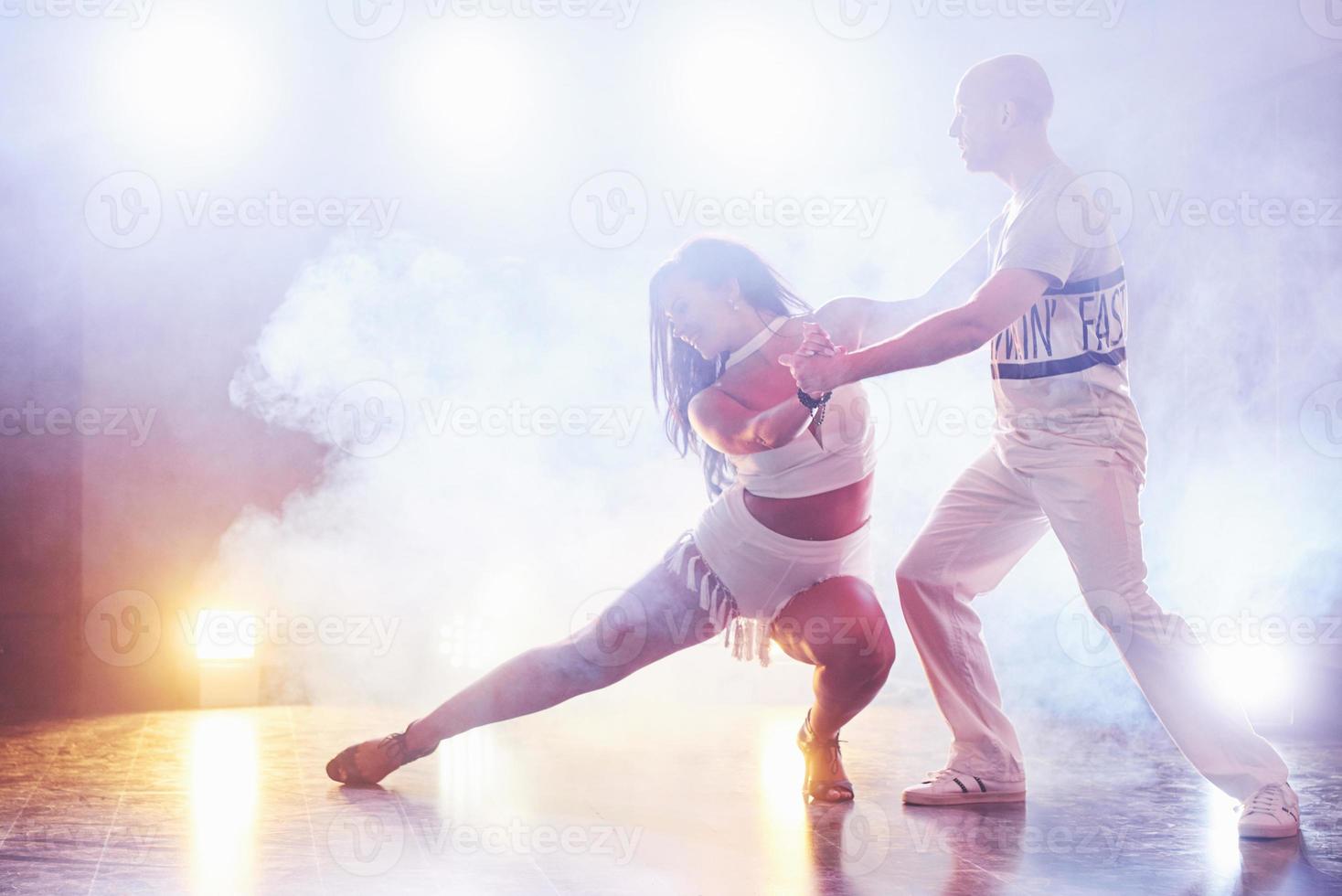 hábiles bailarines actuando en la habitación oscura bajo la luz y el humo del concierto. pareja sensual realizando una danza contemporánea artística y emocional foto