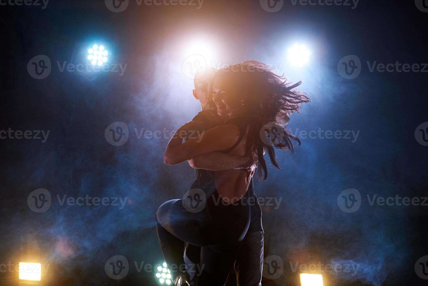 hábiles bailarines actuando en la habitación oscura bajo la luz y el humo del concierto. pareja sensual realizando una danza contemporánea artística y emocional foto