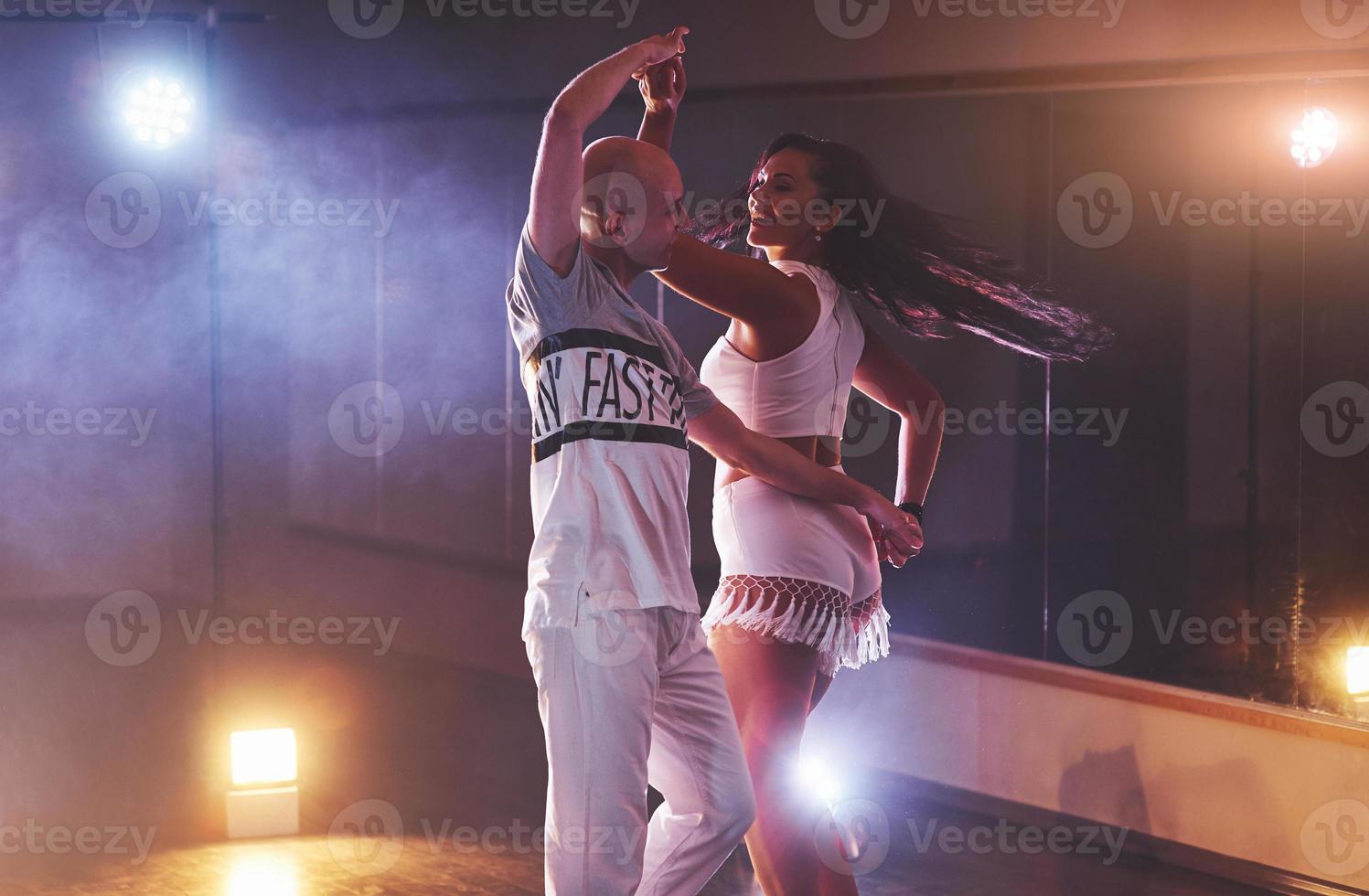 hábiles bailarines actuando en la habitación oscura bajo la luz y el humo del concierto. pareja sensual realizando una danza contemporánea artística y emocional foto