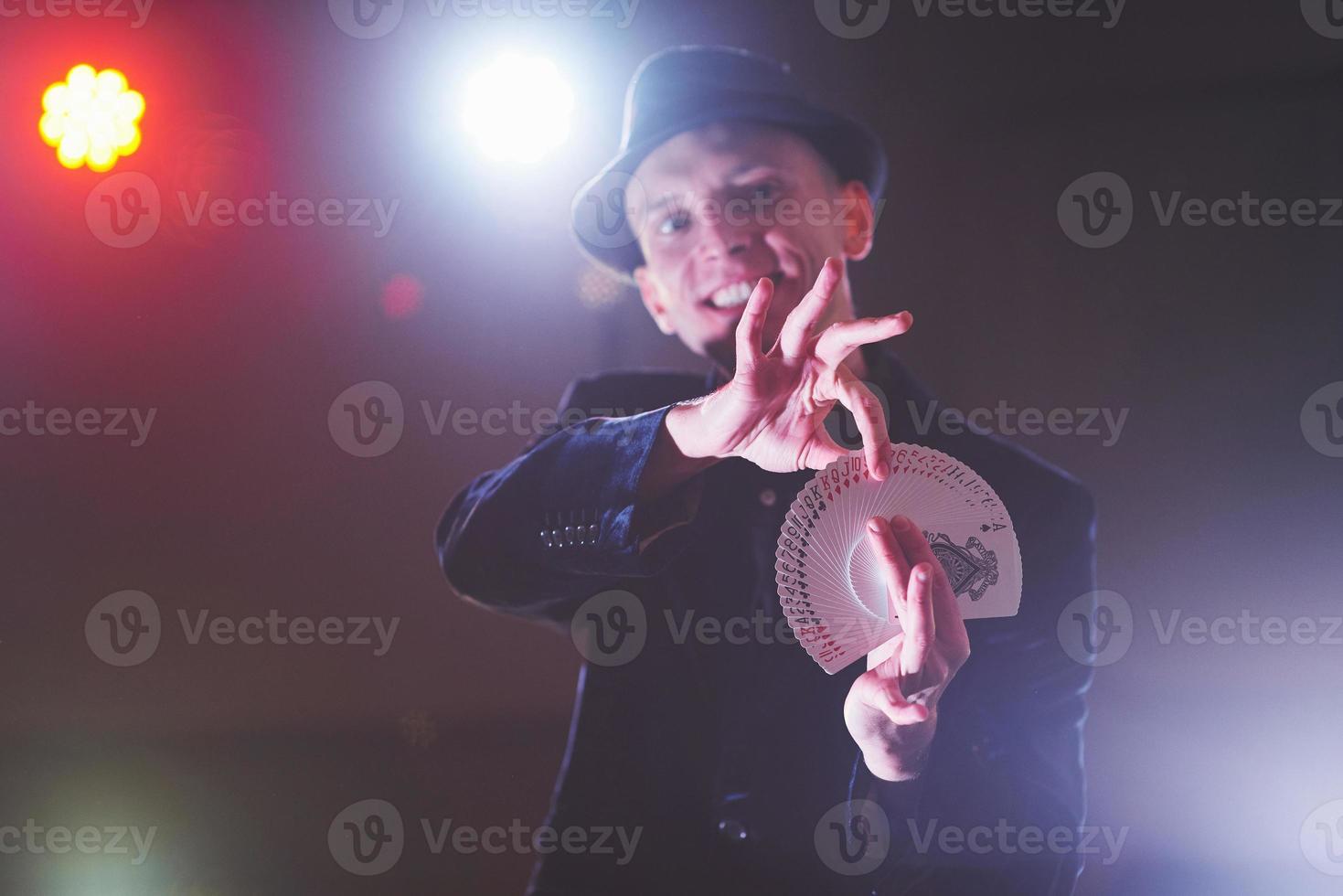 Magician showing trick with playing cards. Magic or dexterity, circus, gambling. Prestidigitator in dark room with fog photo