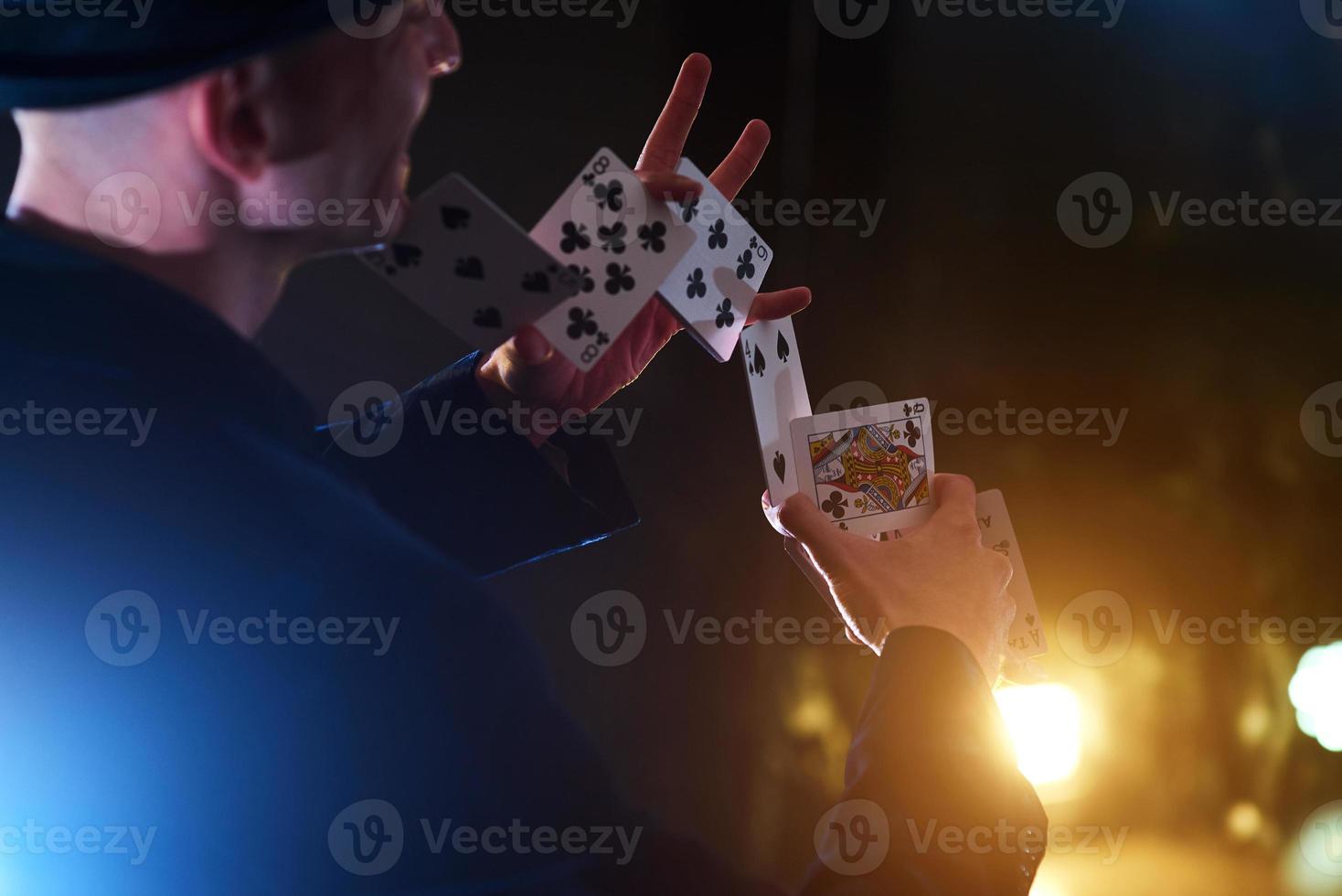 Magician showing trick with playing cards. Magic or dexterity, circus, gambling. Prestidigitator in dark room with fog photo