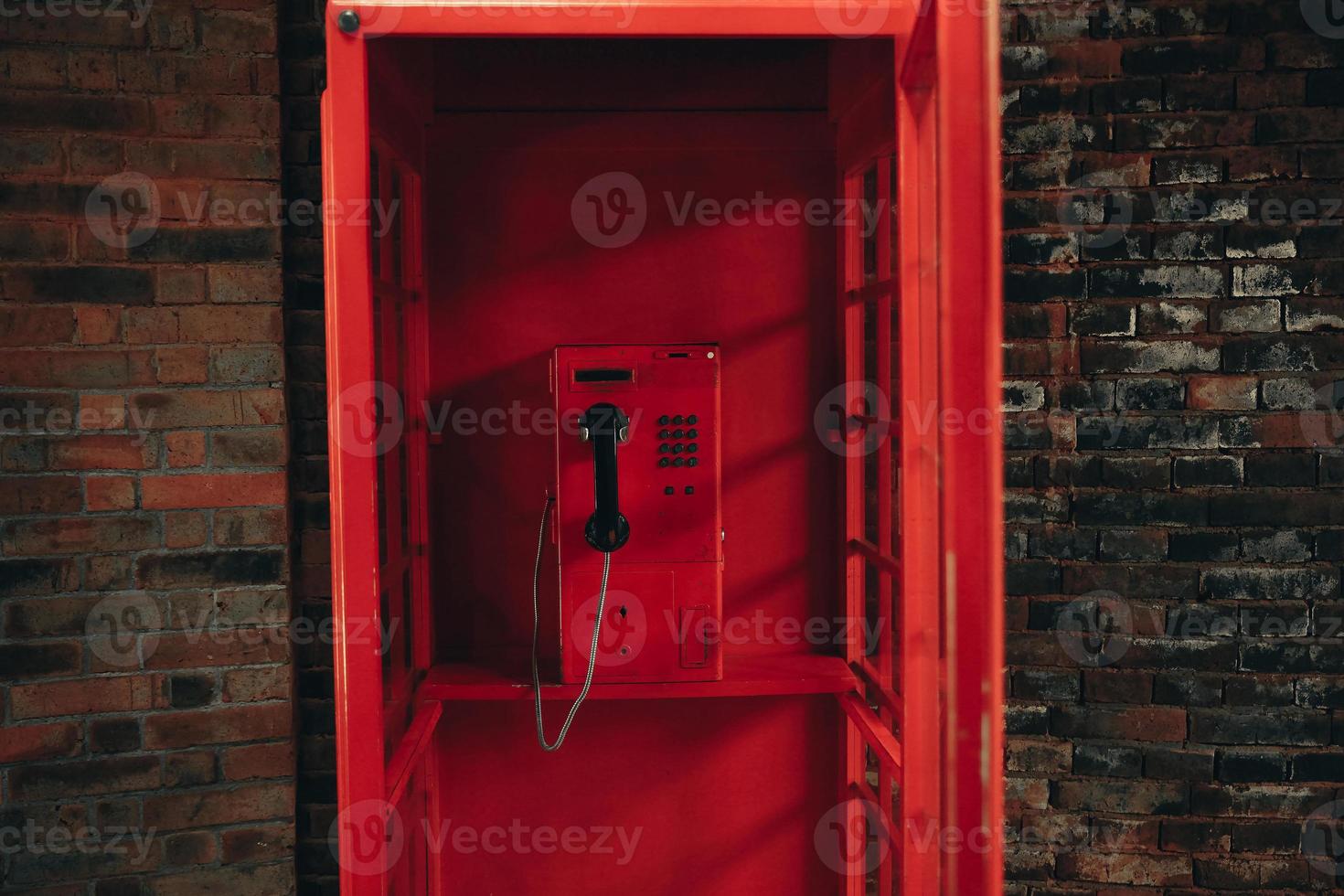 Teléfono público rojo de la vieja escuela dentro de una cabina telefónica roja vintage foto