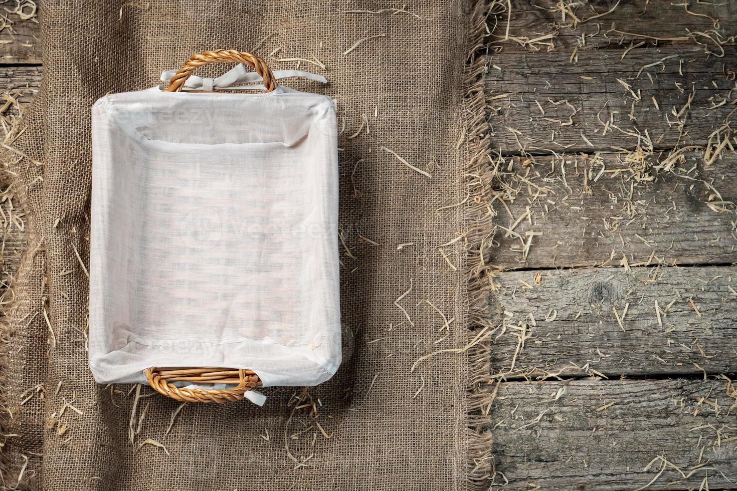 Empty wicker bread basket with white napkin on burlap cloth covered with straw photo