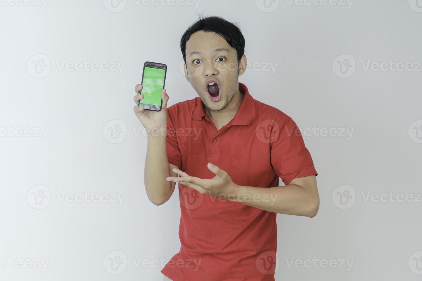 Wow face of Young asian man smiling when showing green screen of smartphone in studio background photo