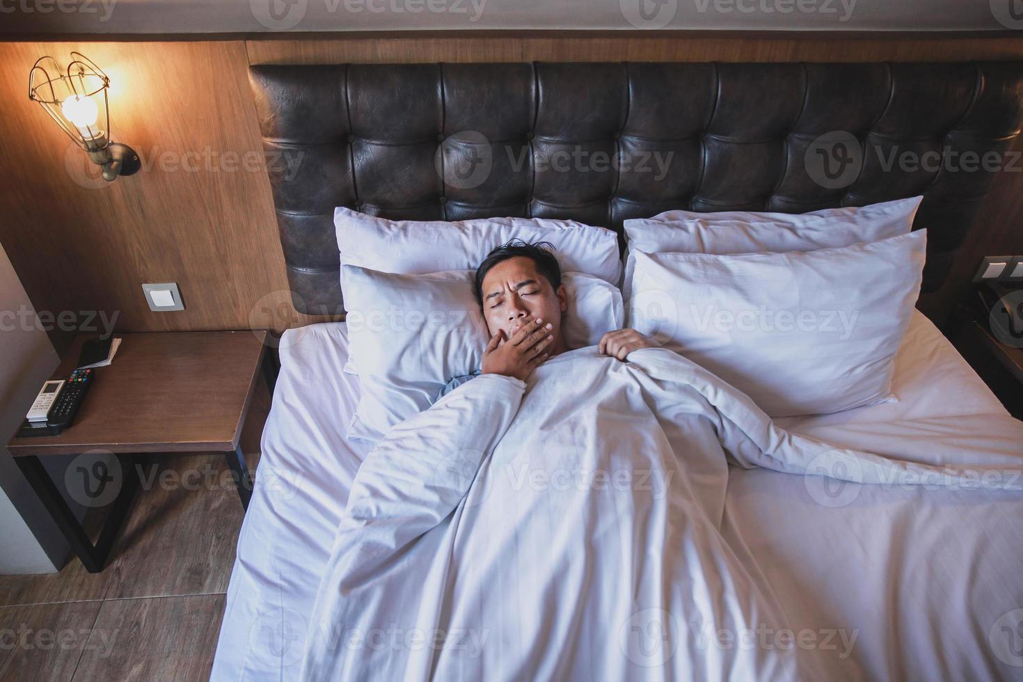 Asian man using blanket yawning while lying on a bed photo