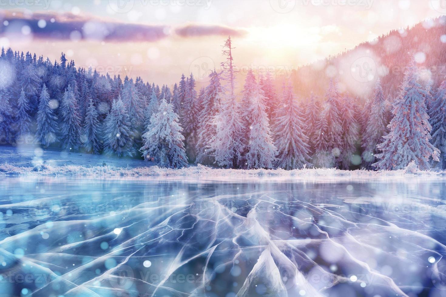 Blue ice and cracks on the surface of the ice. Frozen lake in winter mountains. It is snowing. The hills of pines. Winter. Carpathian Ukraine Europe photo