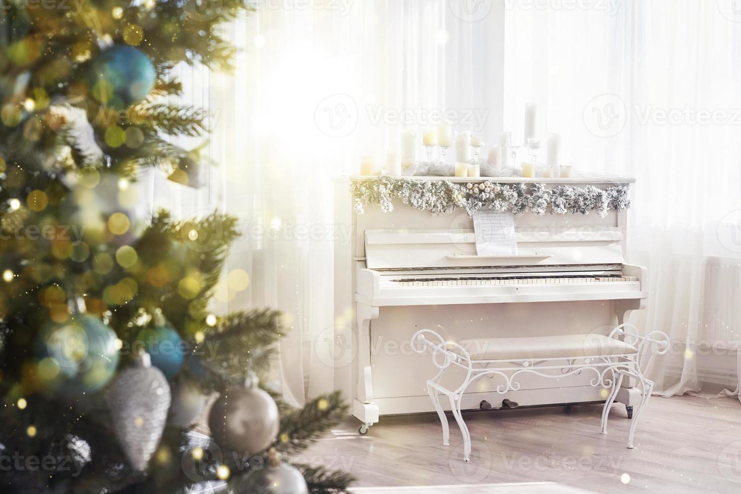 decoración de año nuevo. árbol de navidad cerca de piano blanco en el fondo de la ventana foto