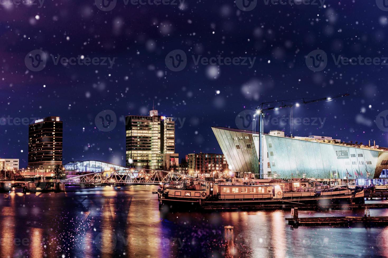 hermosa noche en amsterdam. iluminación nocturna de edificios y barcos cerca del agua en el canal durante una tormenta de nieve. efecto de luz bokeh, filtro suave foto