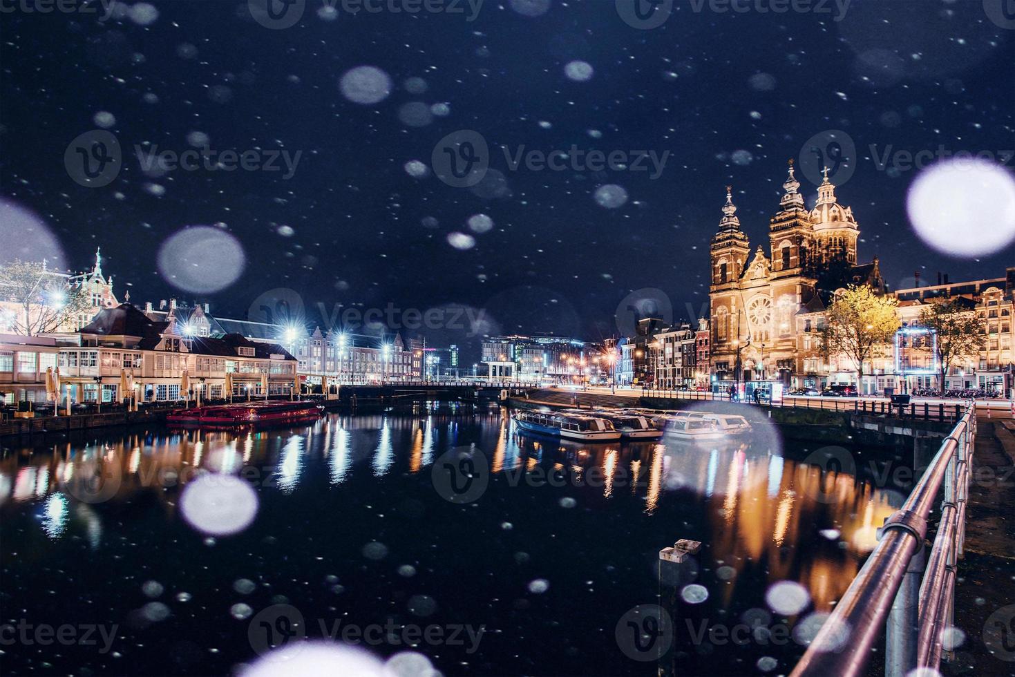 hermosa noche en amsterdam. iluminación nocturna de edificios y barcos cerca del agua en el canal durante una tormenta de nieve. efecto de luz bokeh, filtro suave foto