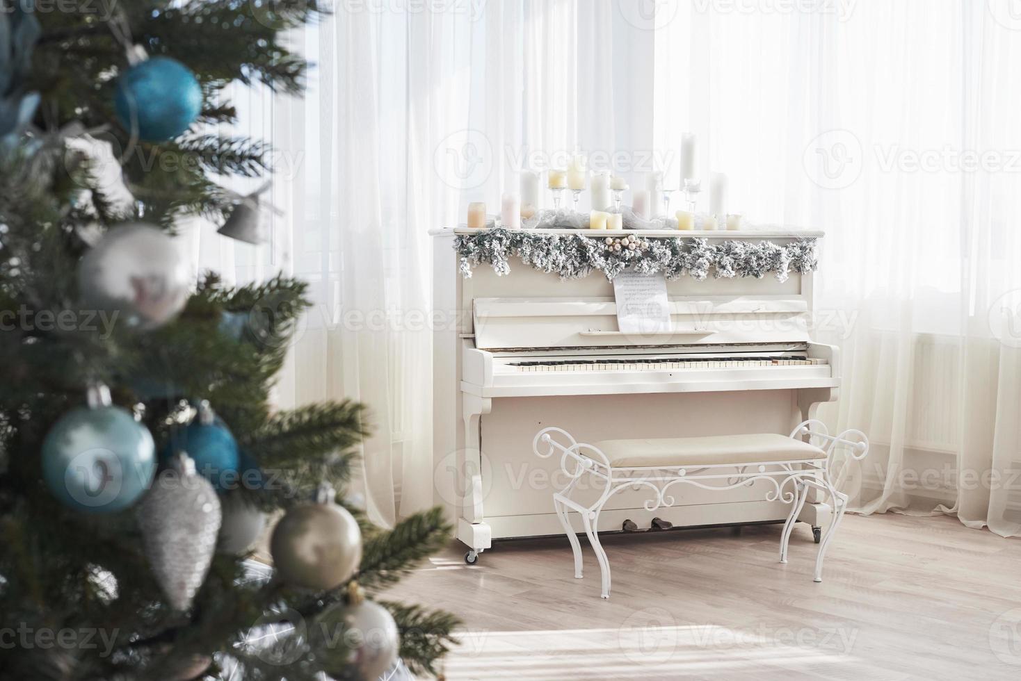 decoración de año nuevo. árbol de navidad cerca de piano blanco en el fondo de la ventana foto