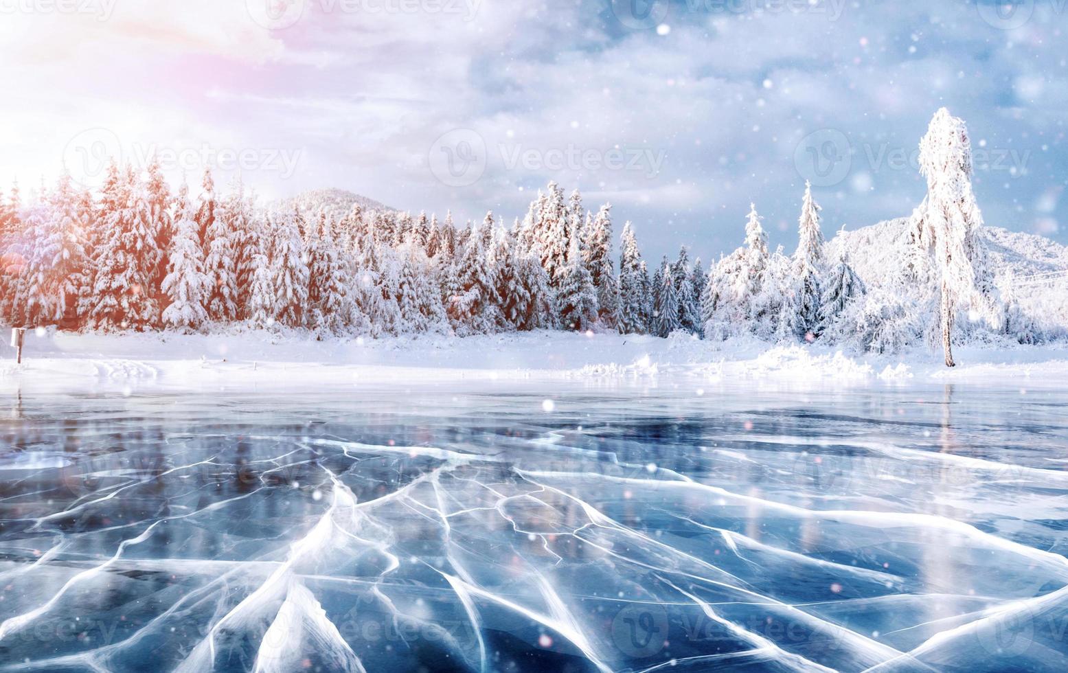 Blue ice and cracks on the surface of the ice. Frozen lake in winter mountains. It is snowing. The hills of pines. Winter. Carpathian Ukraine Europe photo