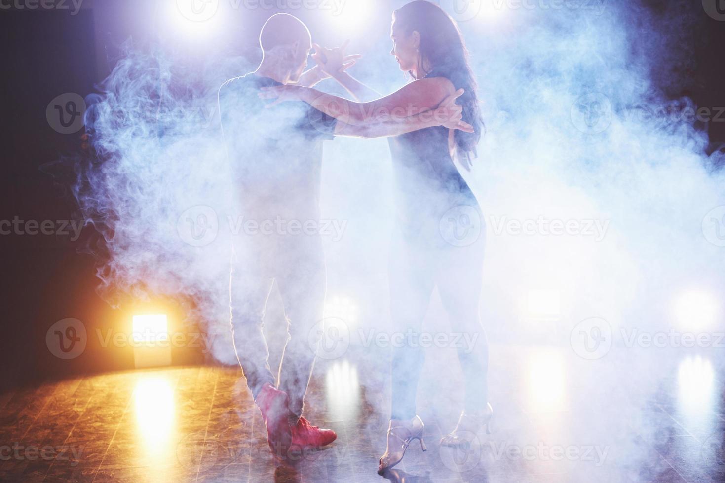 hábiles bailarines actuando en la habitación oscura bajo la luz y el humo del concierto. pareja sensual realizando una danza contemporánea artística y emocional foto