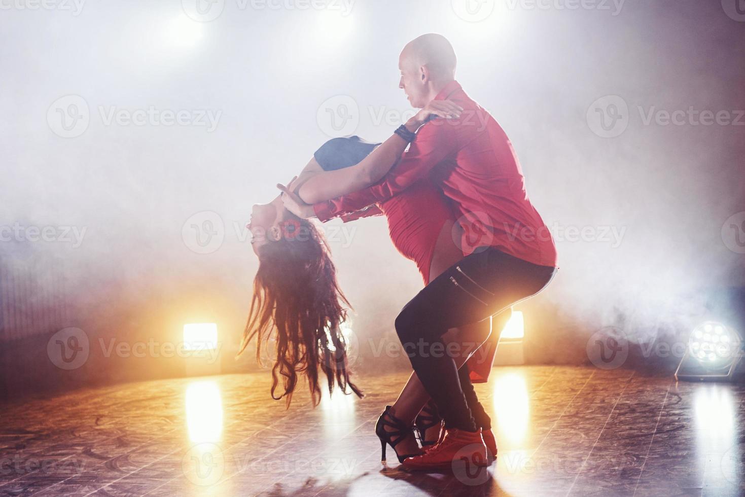 hábiles bailarines actuando en la habitación oscura bajo la luz y el humo del concierto. pareja sensual realizando una danza contemporánea artística y emocional foto