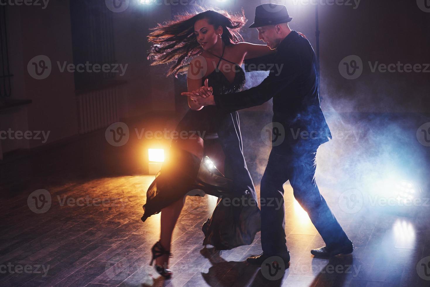 hábiles bailarines actuando en la habitación oscura bajo la luz y el humo del concierto. pareja sensual realizando una danza contemporánea artística y emocional foto