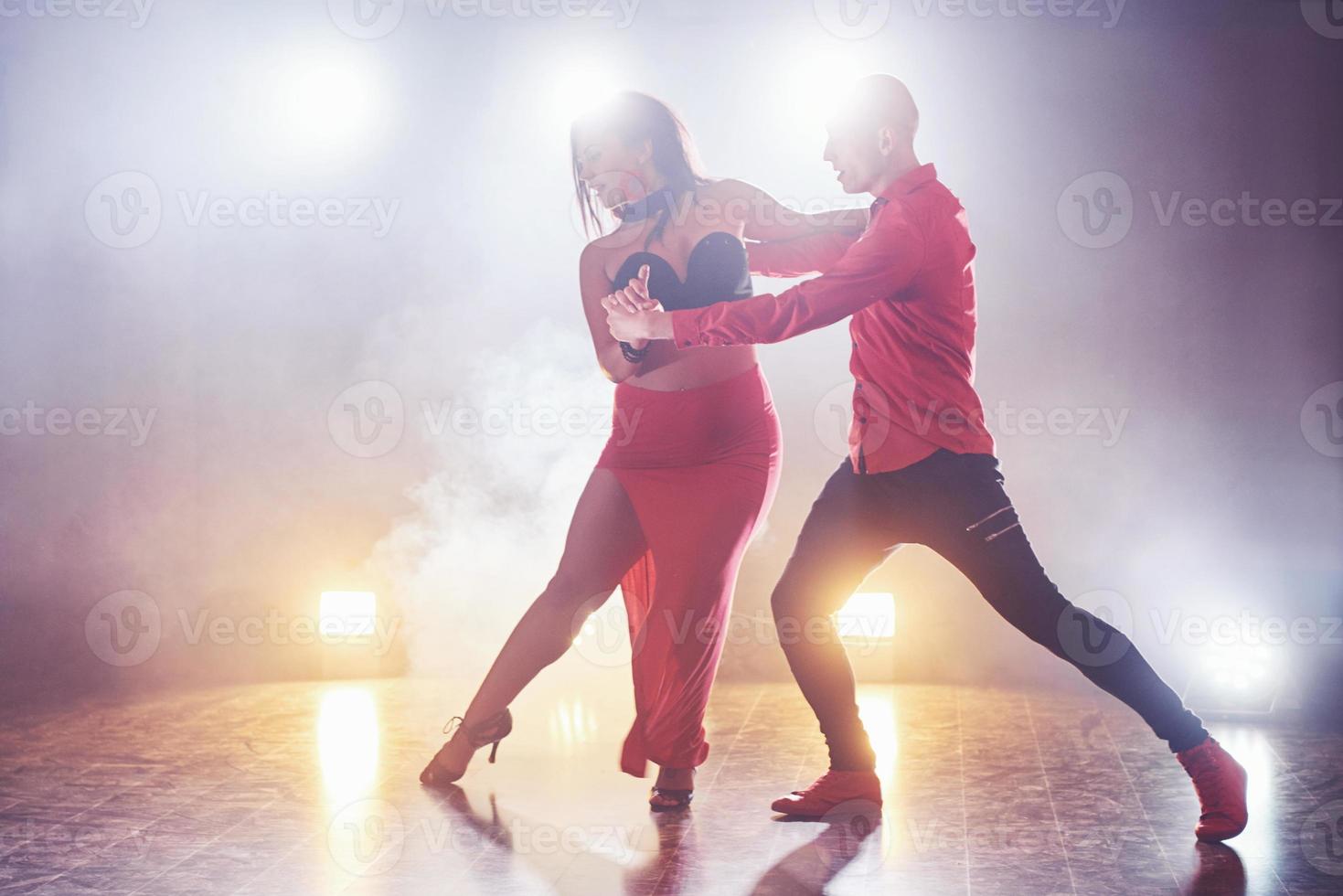 hábiles bailarines actuando en la habitación oscura bajo la luz y el humo del concierto. pareja sensual realizando una danza contemporánea artística y emocional foto