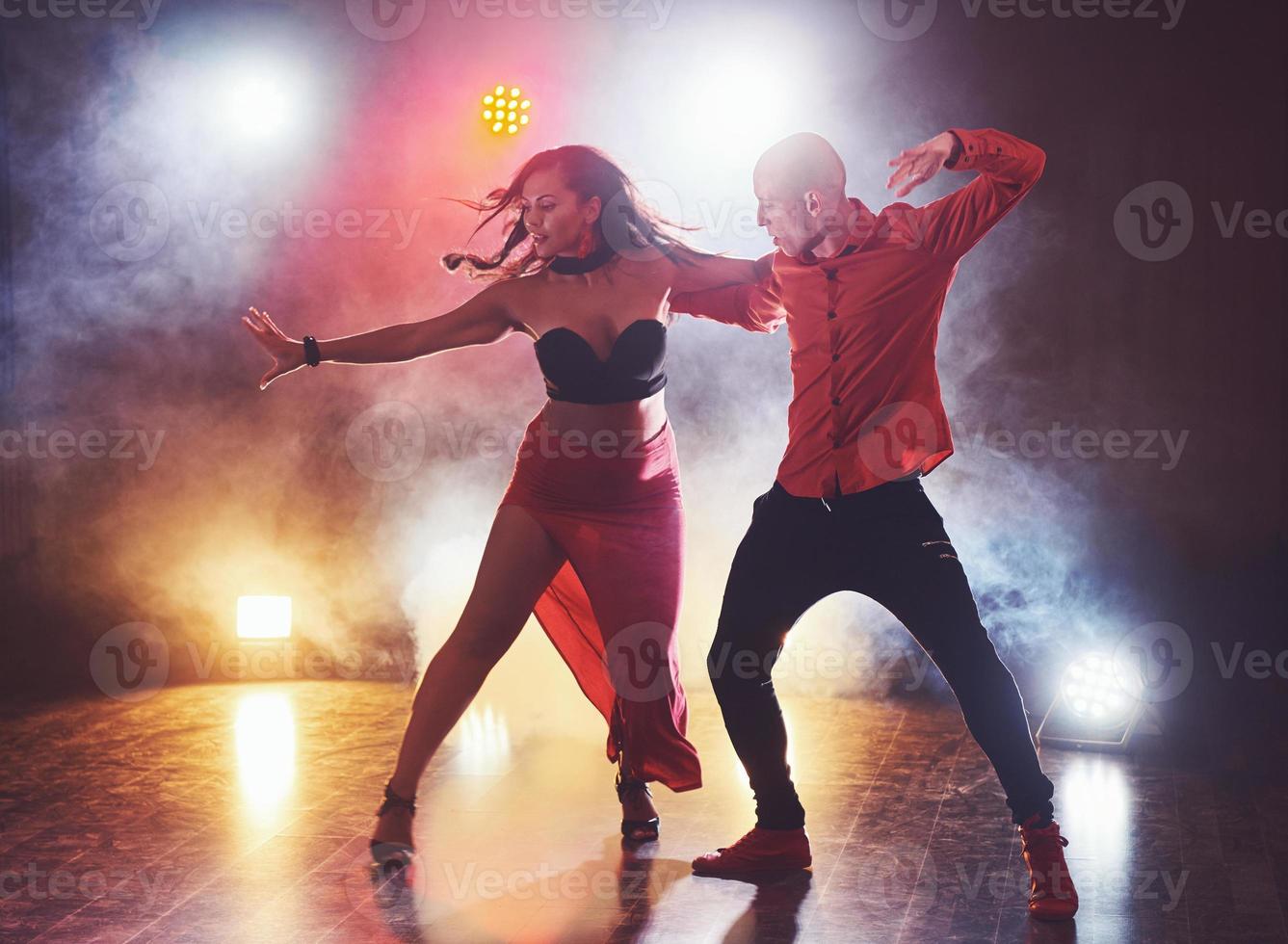 hábiles bailarines actuando en la habitación oscura bajo la luz y el humo del concierto. pareja sensual realizando una danza contemporánea artística y emocional foto