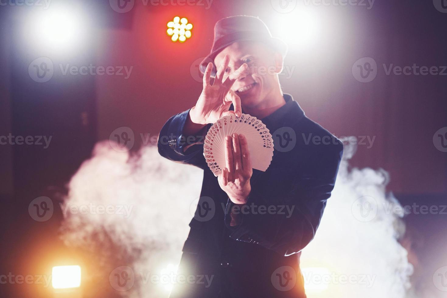 Magician showing trick with playing cards. Magic or dexterity, circus, gambling. Prestidigitator in dark room with fog photo