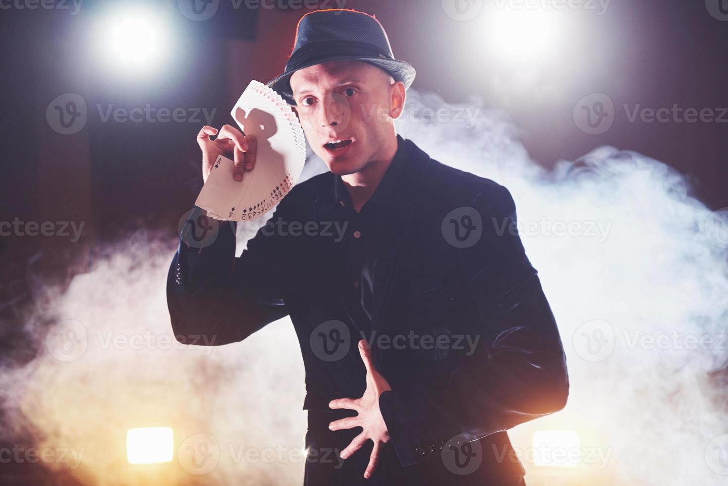 Magician showing trick with playing cards. Magic or dexterity, circus, gambling. Prestidigitator in dark room with fog photo