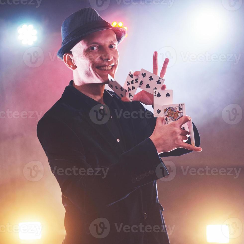 Magician showing trick with playing cards. Magic or dexterity, circus, gambling. Prestidigitator in dark room with fog photo