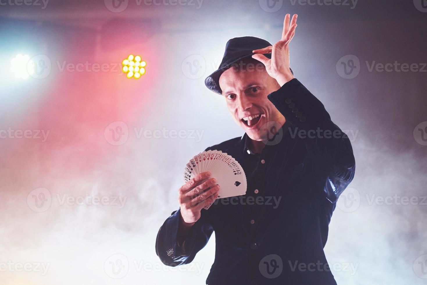 Magician showing trick with playing cards. Magic or dexterity, circus, gambling. Prestidigitator in dark room with fog photo