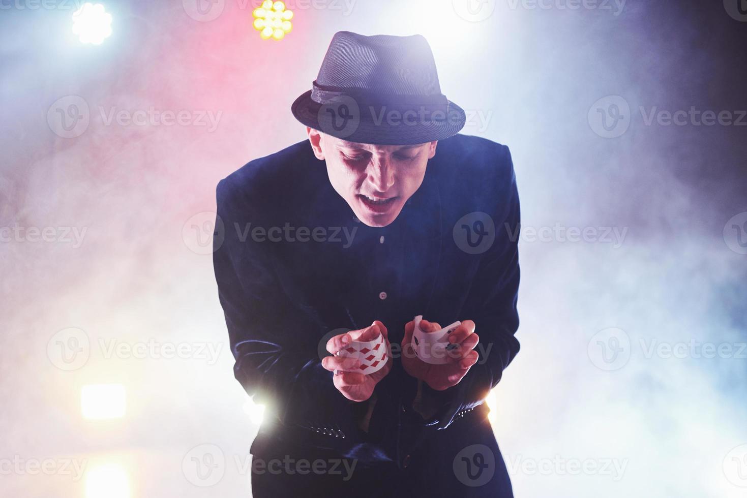 Magician showing trick with playing cards. Magic or dexterity, circus, gambling. Prestidigitator in dark room with fog photo