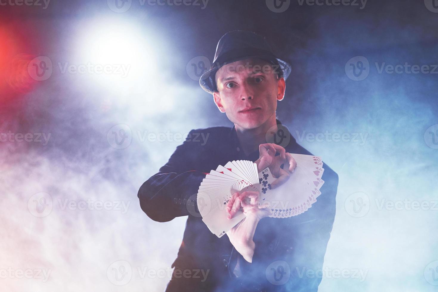 Magician showing trick with playing cards. Magic or dexterity, circus, gambling. Prestidigitator in dark room with fog photo