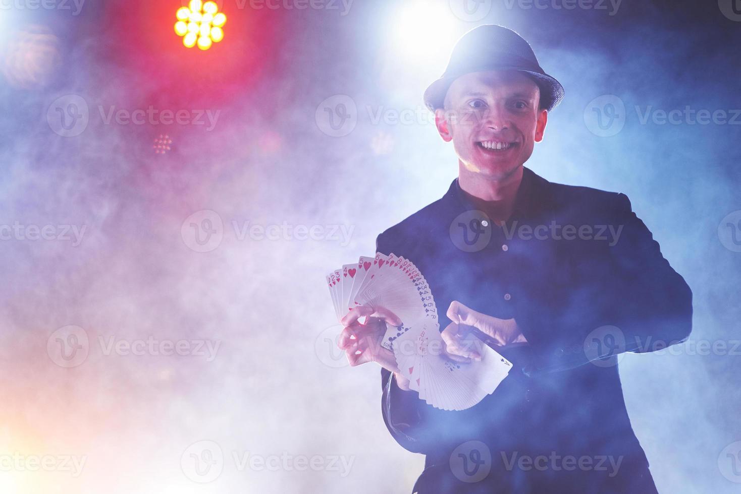 Magician showing trick with playing cards. Magic or dexterity, circus, gambling. Prestidigitator in dark room with fog photo