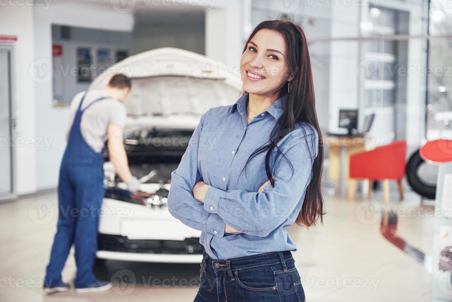 mujer en un garaje de automóviles recibiendo servicio mecánico. el mecánico trabaja bajo el capó del coche foto