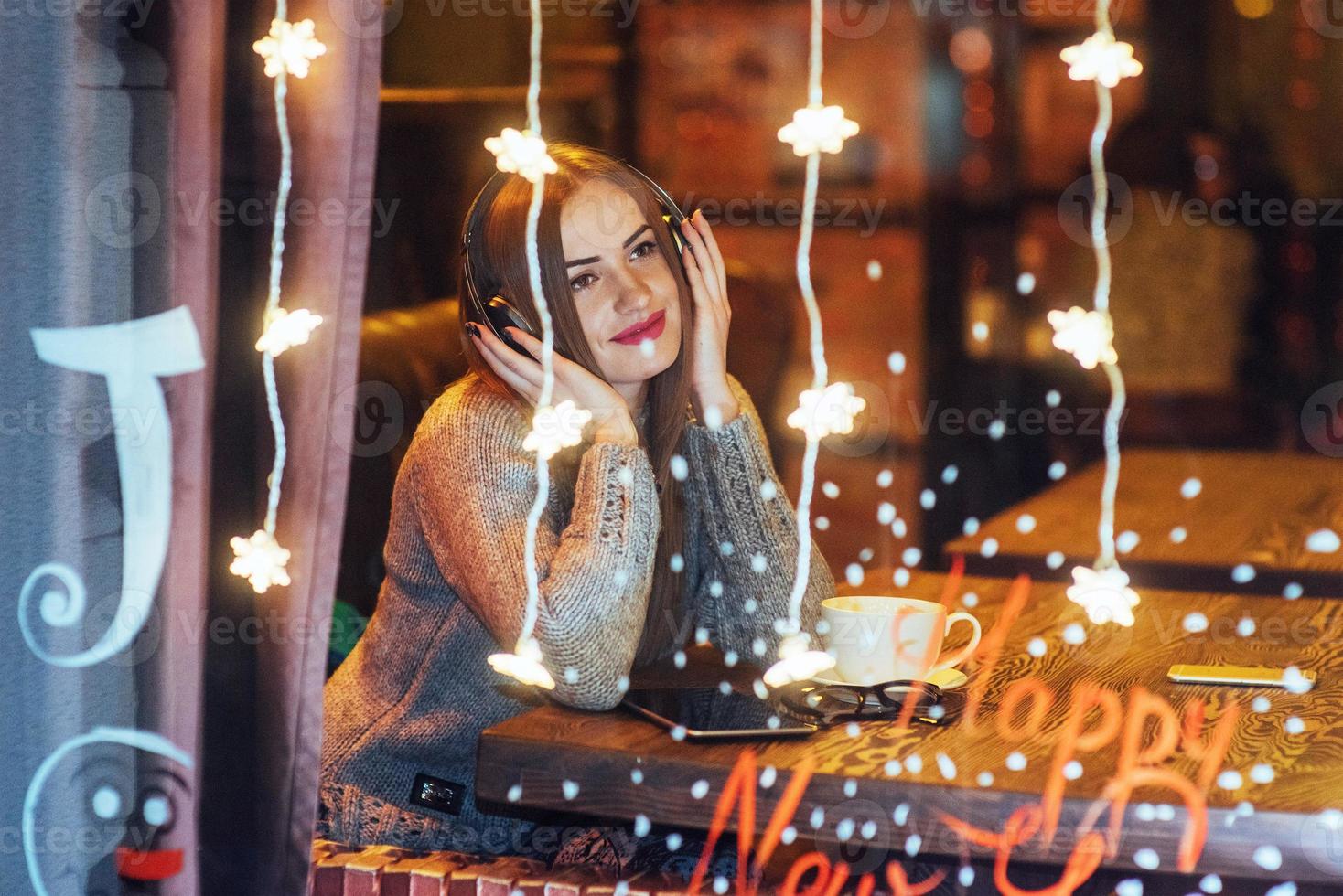 Young beautiful woman sitting in cafe, drinking coffee. Model listening to music. Christmas, Happy new year, Valentines day, winter holidays concept photo