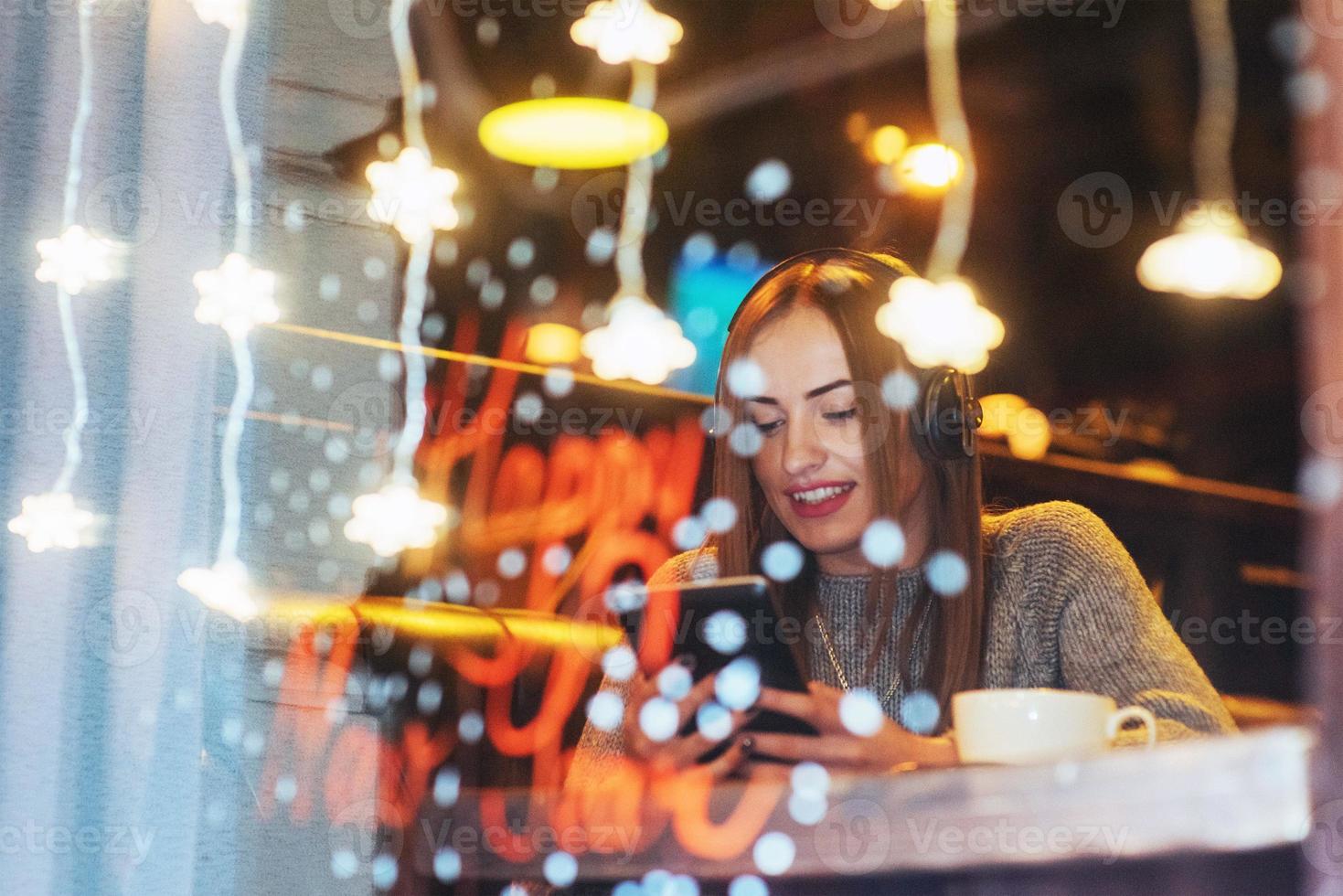Young beautiful woman sitting in cafe, drinking coffee. Model listening to music. Christmas, Happy new year, Valentines day, winter holidays concept photo