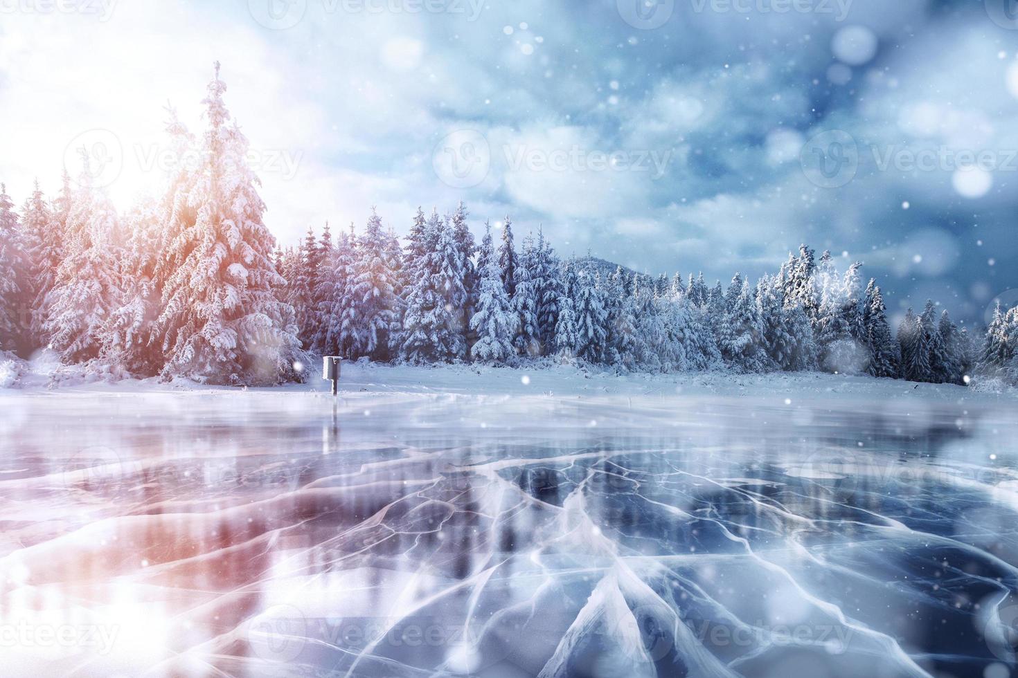 Blue ice and cracks on the surface of the ice. Frozen lake in winter mountains. It is snowing. The hills of pines. Winter. Carpathian Ukraine Europe photo