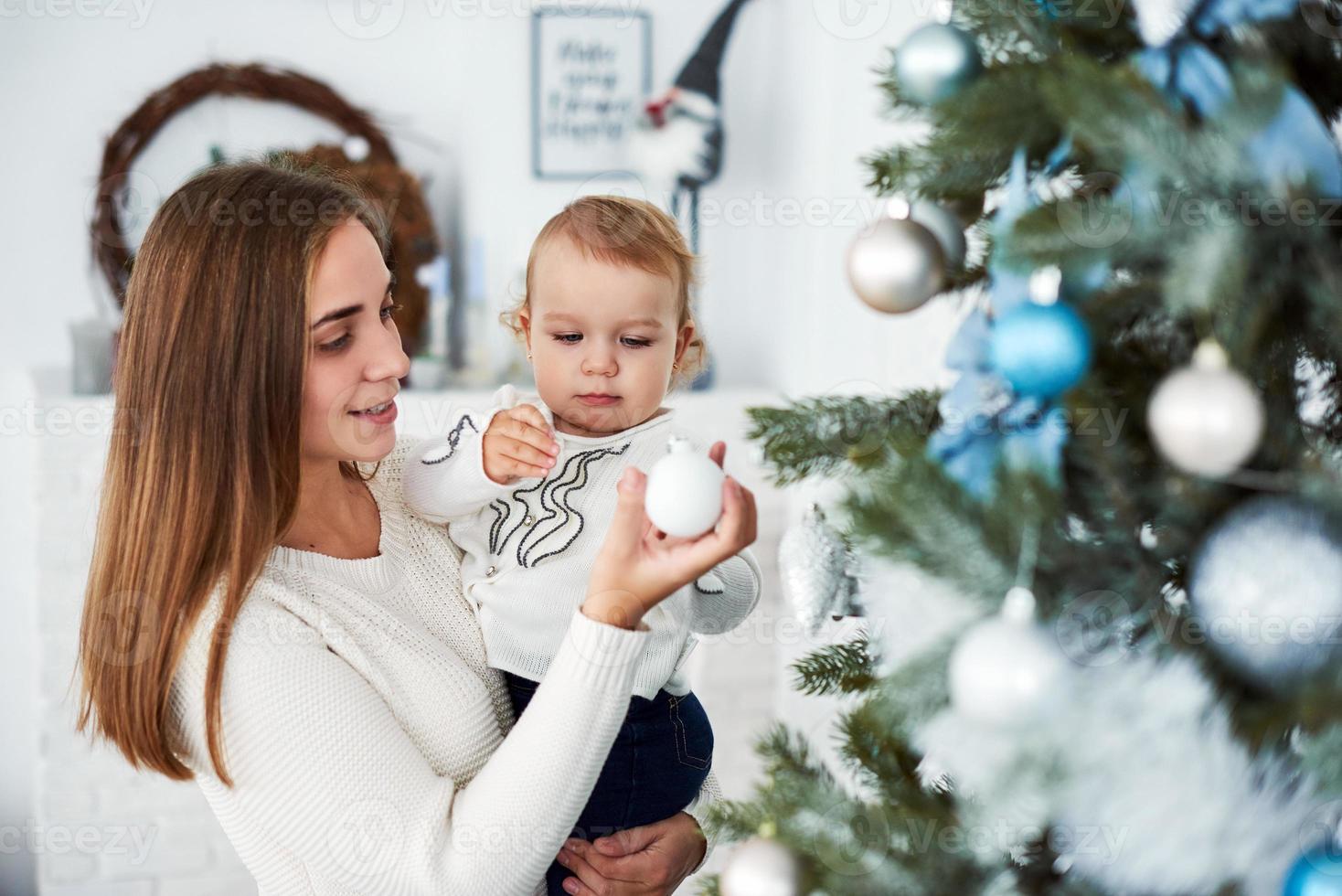 feliz madre de familia y el bebé decoran el árbol de navidad foto