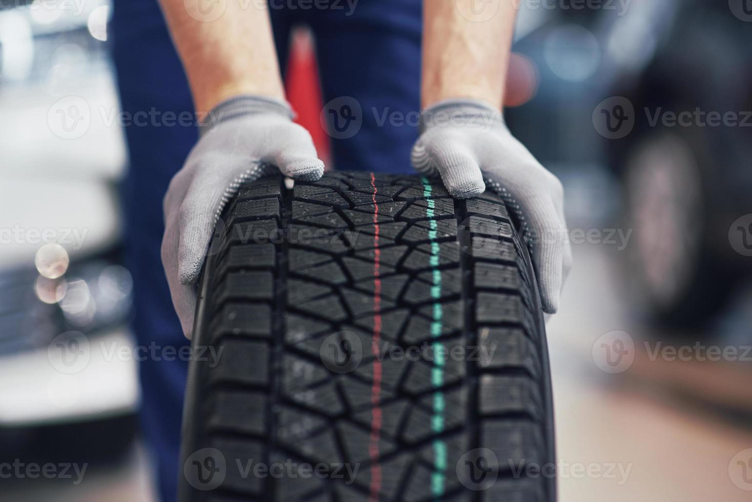 Closeup of mechanic hands pushing a black tire in the workshop photo
