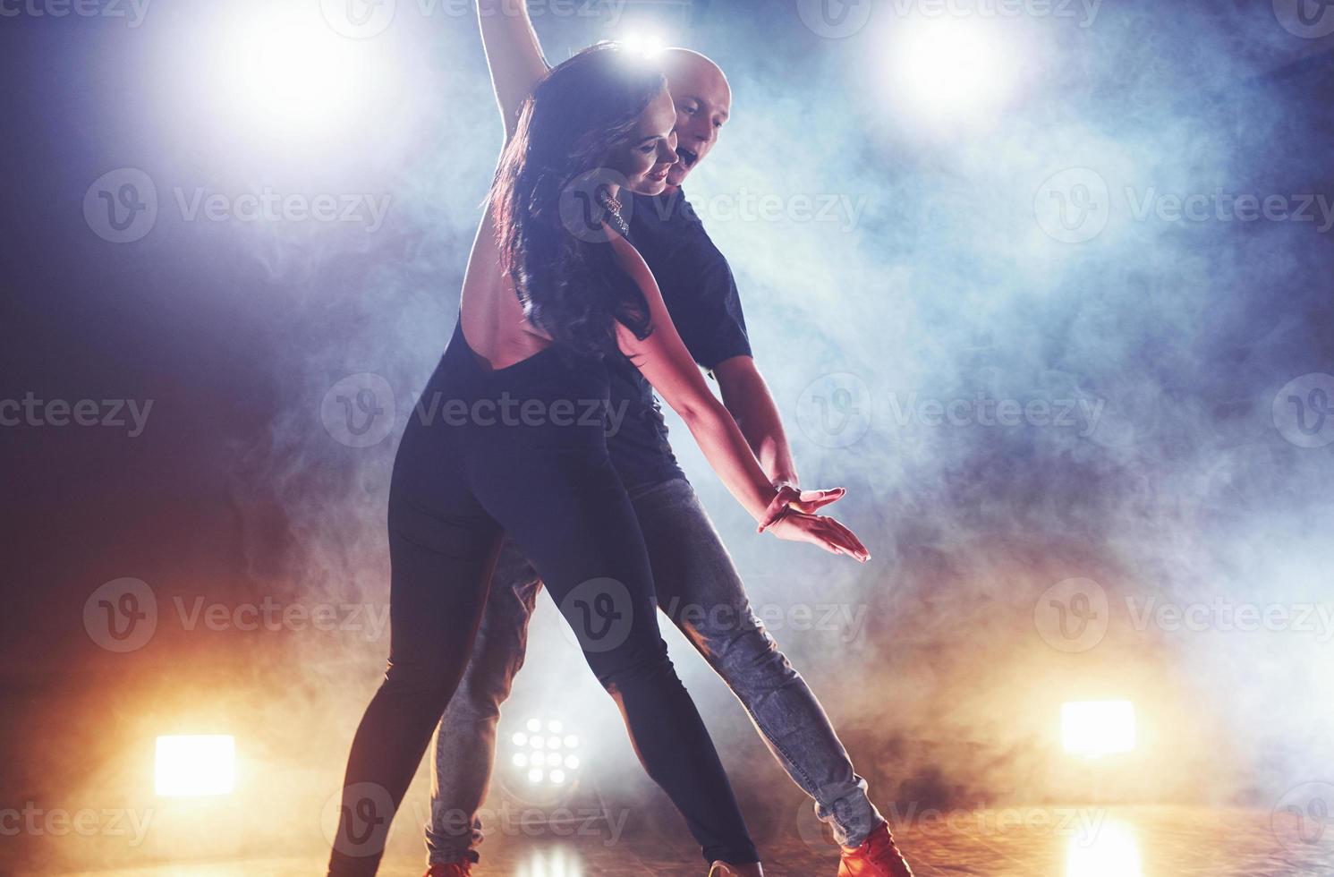 Skillful dancers performing in the dark room under the concert light and smoke. Sensual couple performing an artistic and emotional contemporary dance photo