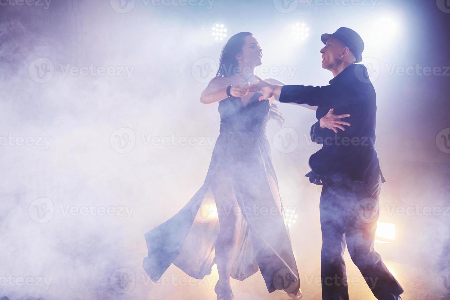 hábiles bailarines actuando en la habitación oscura bajo la luz y el humo del concierto. pareja sensual realizando una danza contemporánea artística y emocional foto