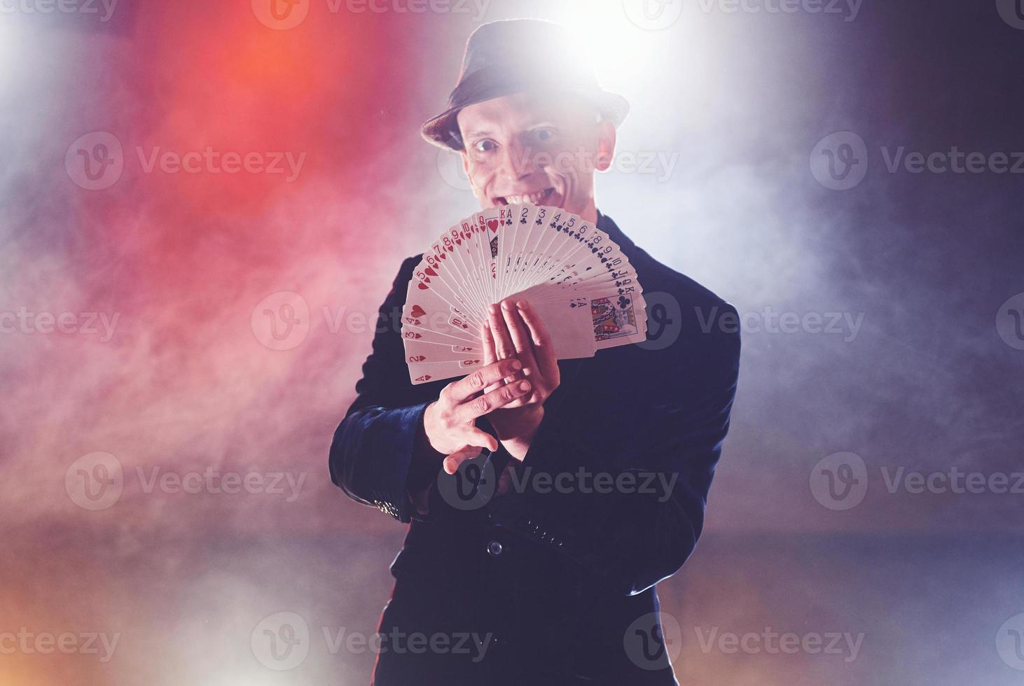 mago mostrando truco con naipes. magia o destreza, circo, juegos de azar. prestidigitador en cuarto oscuro con niebla foto
