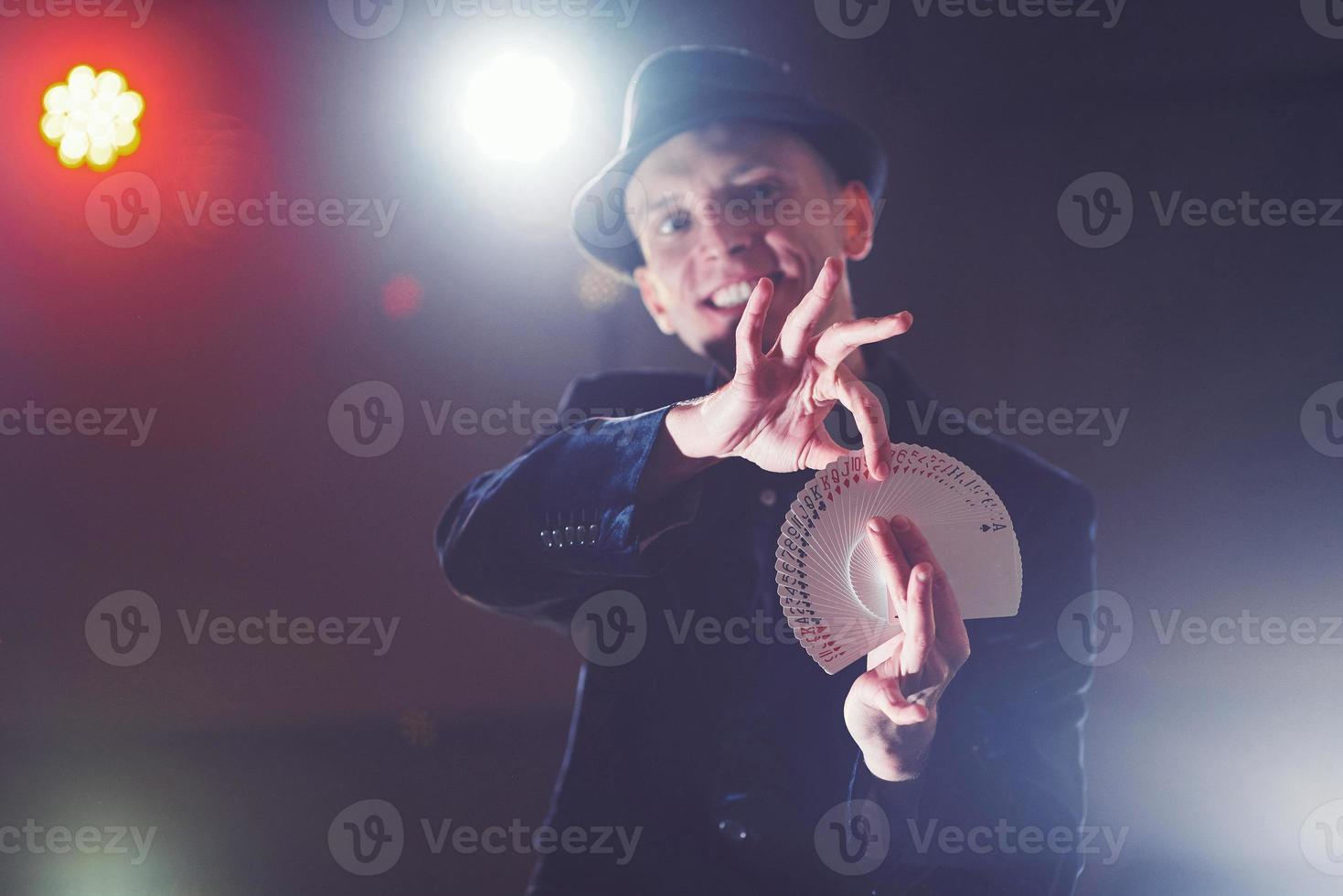 Magician showing trick with playing cards. Magic or dexterity, circus, gambling. Prestidigitator in dark room with fog photo