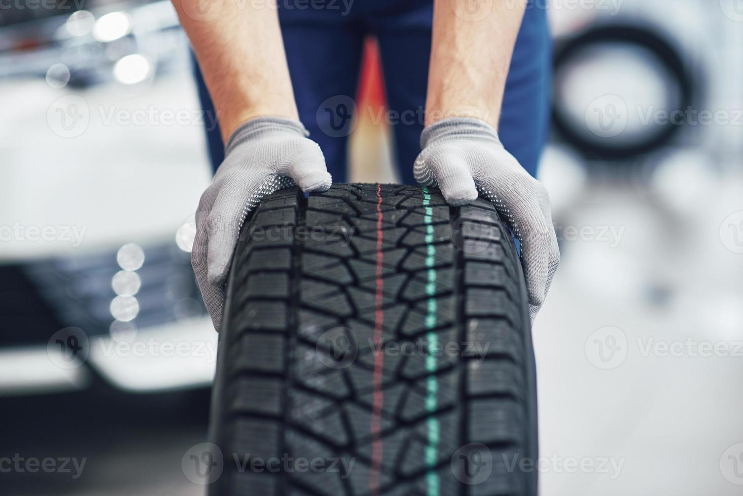 Closeup of mechanic hands pushing a black tire in the workshop photo