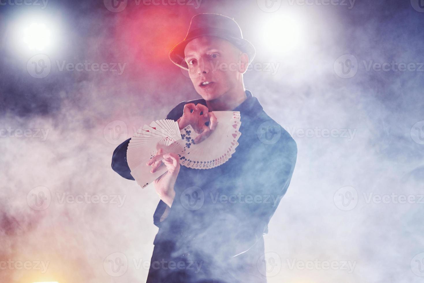 Magician showing trick with playing cards. Magic or dexterity, circus, gambling. Prestidigitator in dark room with fog photo