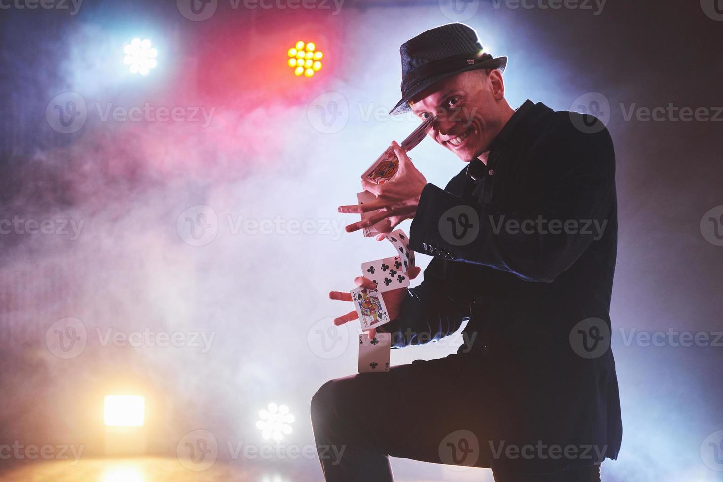 Magician showing trick with playing cards. Magic or dexterity, circus, gambling. Prestidigitator in dark room with fog photo