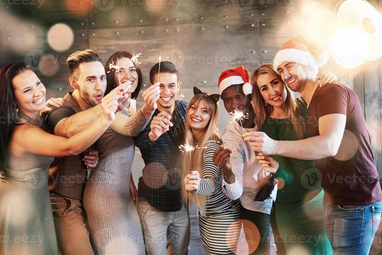 Party with friends. Group of cheerful young people carrying sparklers and champagne flutes. Bokeh light soft effect. photo