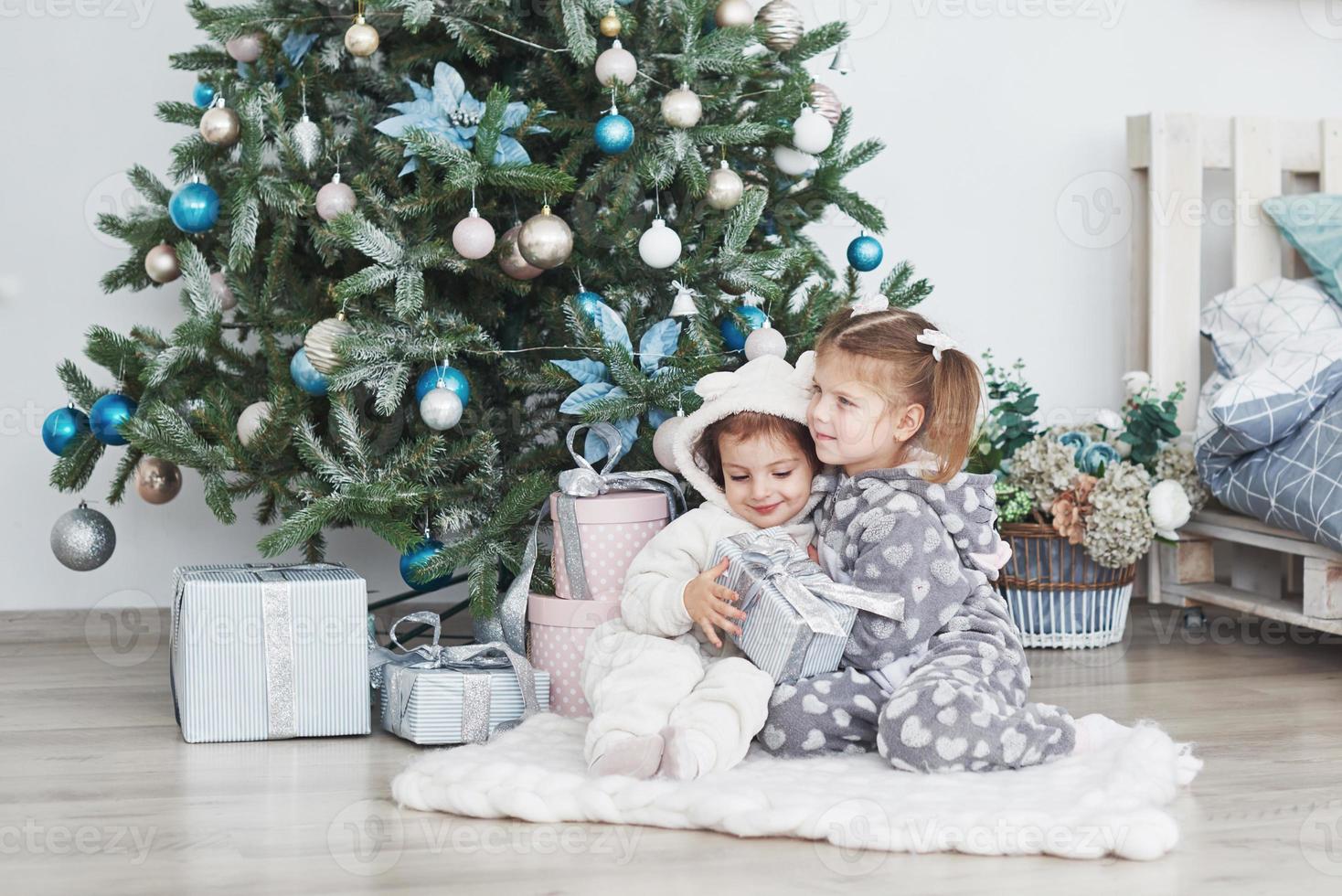 Two little sister girls open their gifts at the Christmas tree in the morning on the deck photo